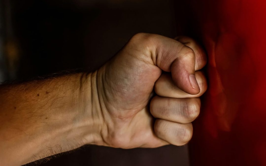 Close-up of a clenched fist against a dark red background, symbolizing anger