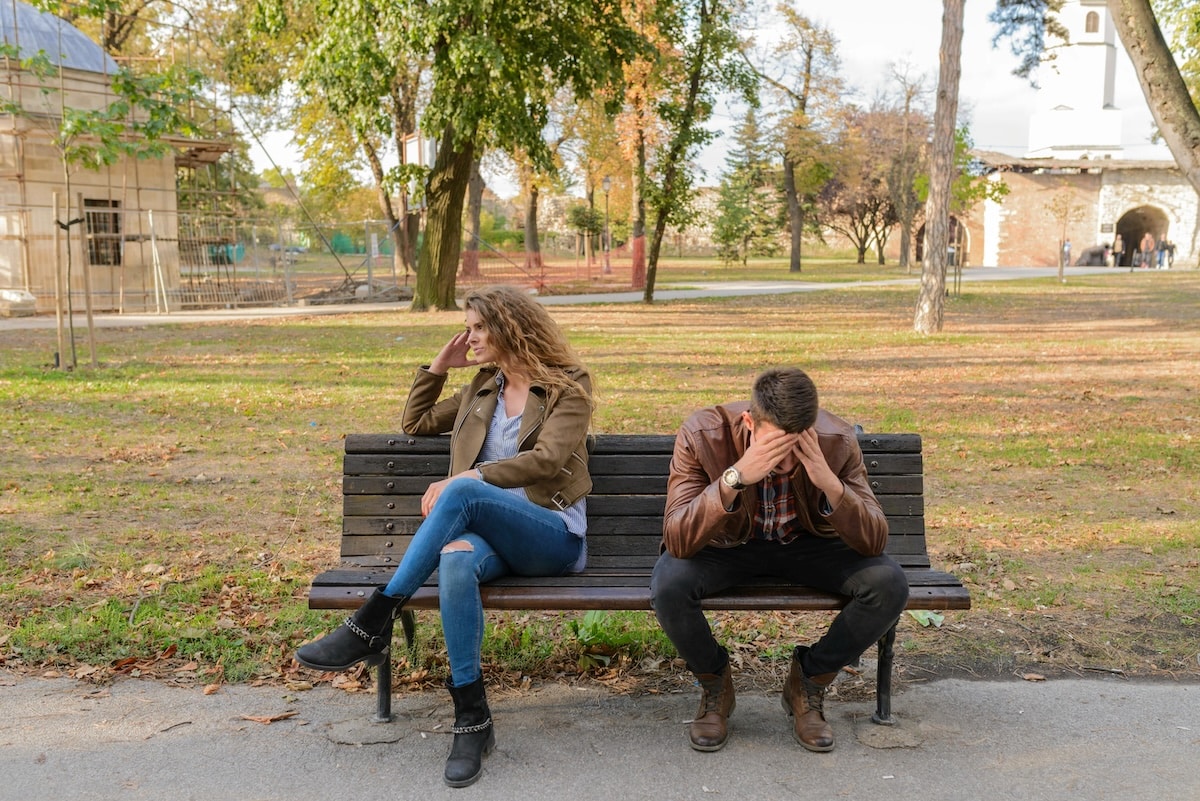 Man and woman sitting apart on a park bench after a breakup, showing emotional distance, grief, and relationship distress