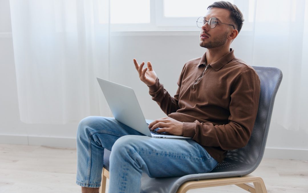 Man seated with a laptop, gesturing while talking during an online therapy session