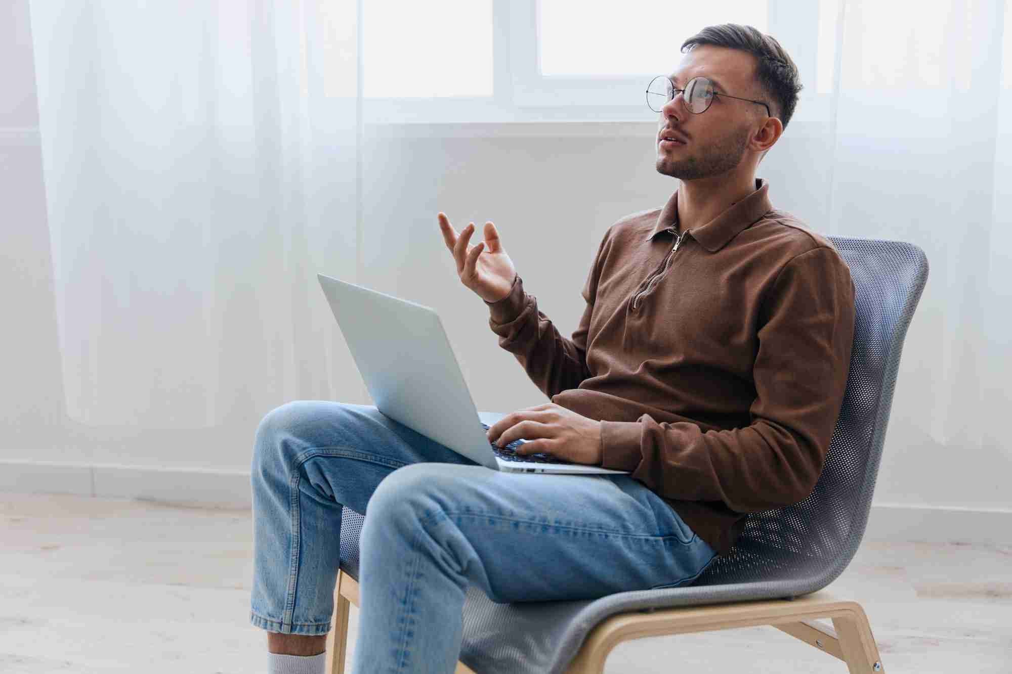 Man seated with a laptop, gesturing while talking during an online therapy session