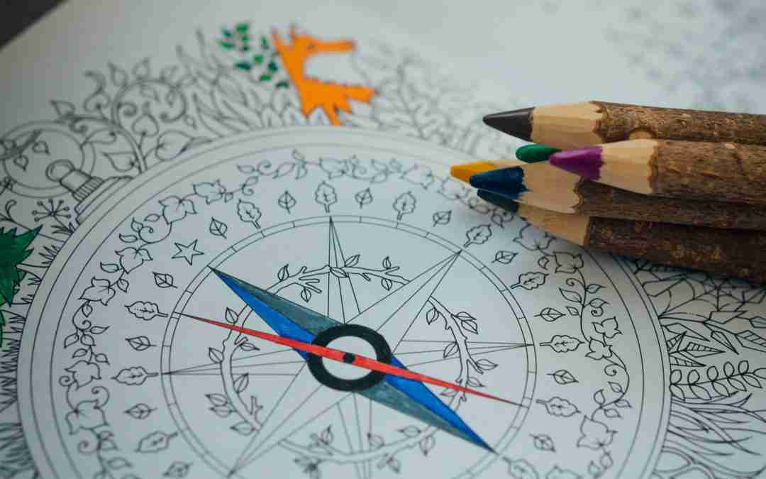 A hand-illustrated compass design in a coloring book, surrounded by colored pencils, symbolizing personal exploration of type and identity